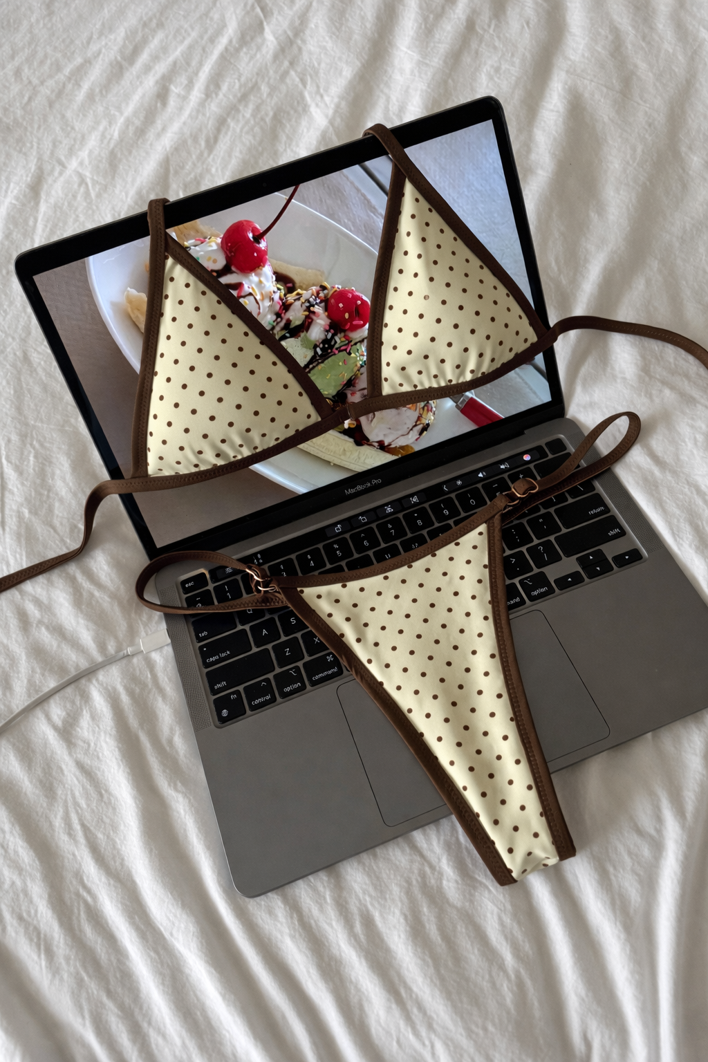 Light yellow triangle bikini top with brown polka dots and brown trim laid flat on laptop keyboard with ice cream photo background
