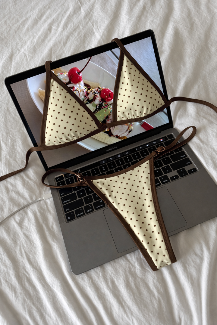 Light yellow triangle bikini top with brown polka dots and brown trim laid flat on laptop keyboard with ice cream photo background