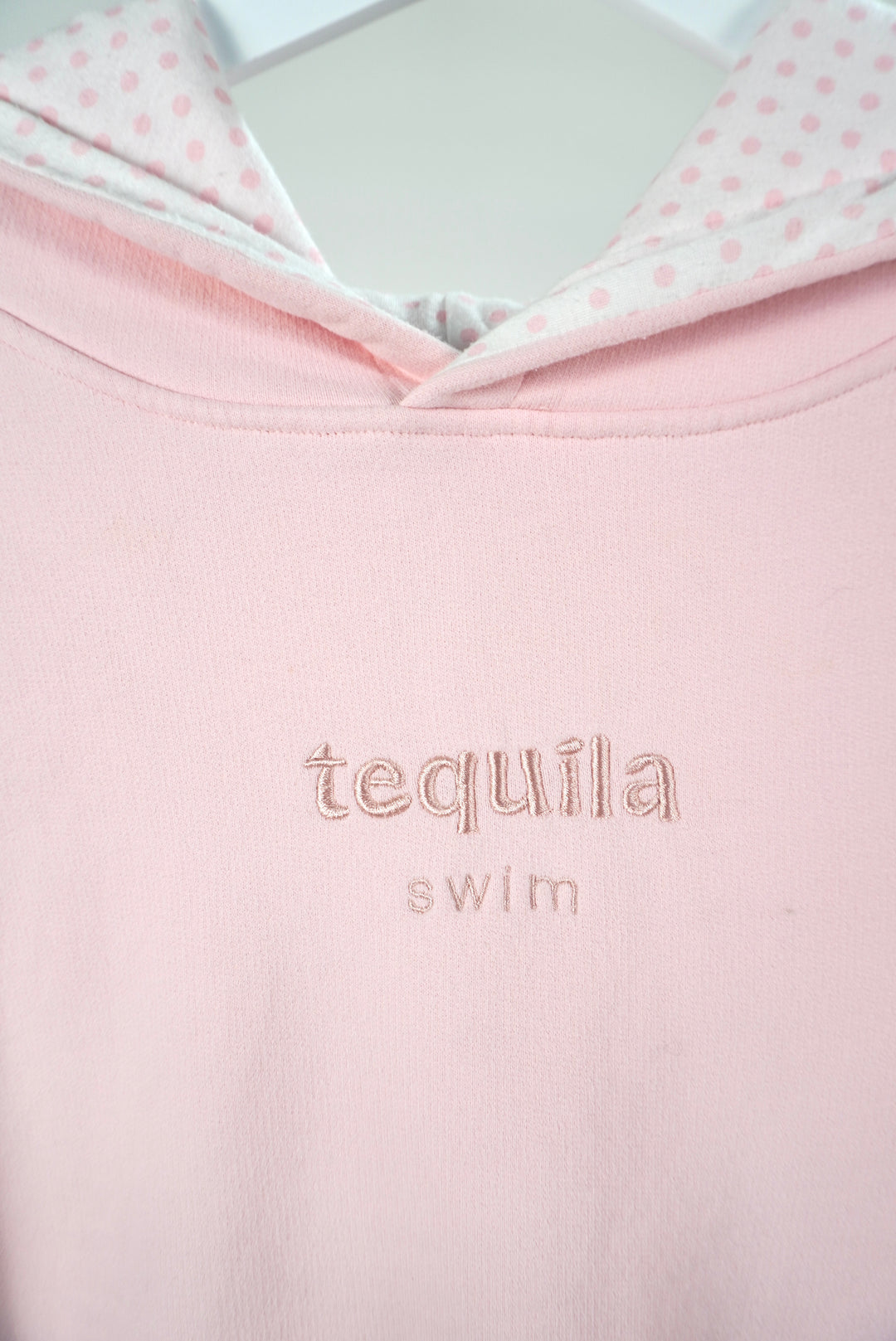 Close-up of a pink Bunny Hug Hoodie with embroidered "tequila swim" text and white hood lining with pink polka dots