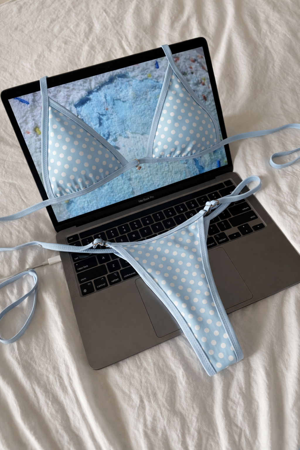 Light blue bikini set with white polka dots and adjustable string ties displayed on open laptop over white fabric background