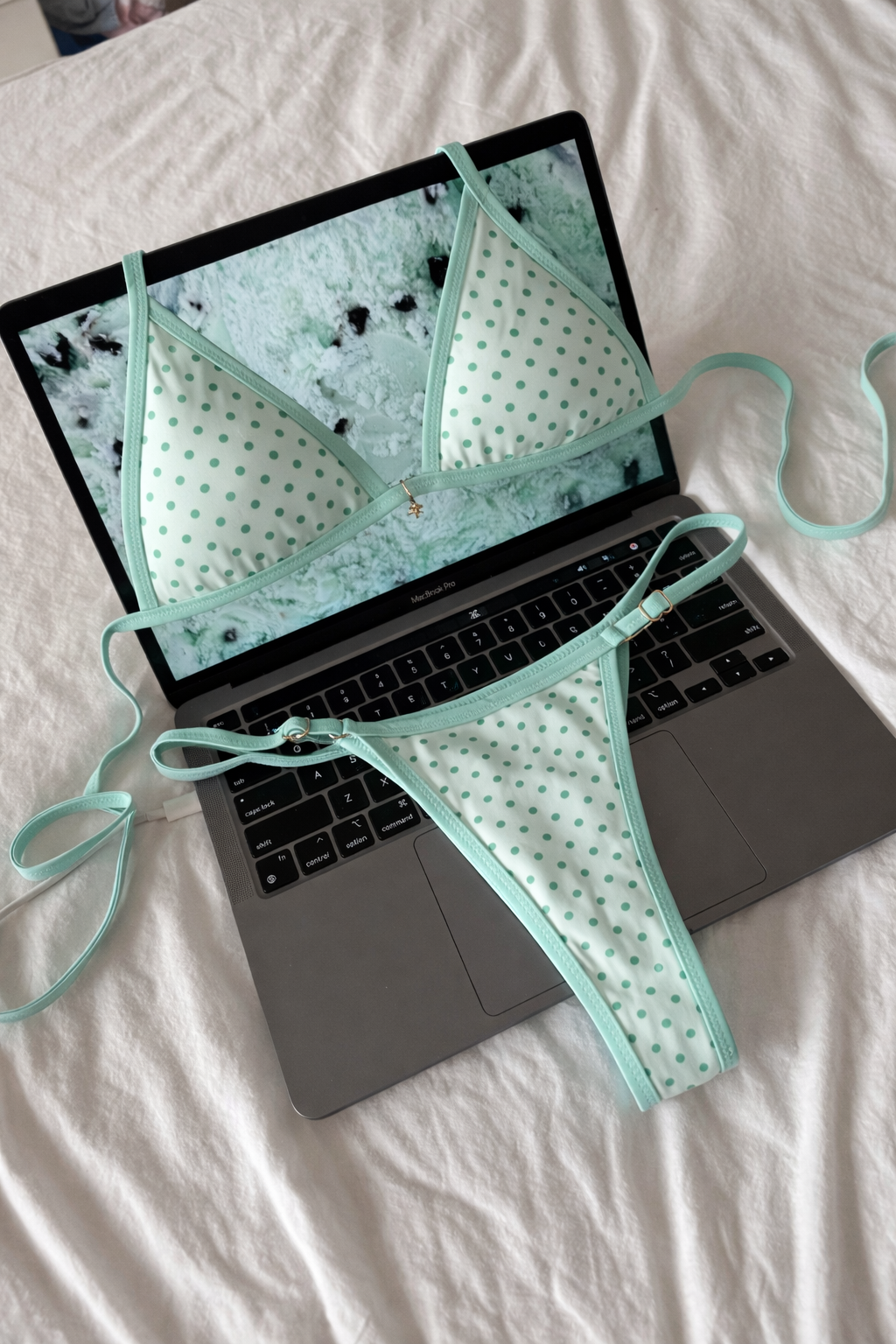 Light green polka dot triangle bikini top and matching thong bottom with thin straps laid flat on laptop keyboard