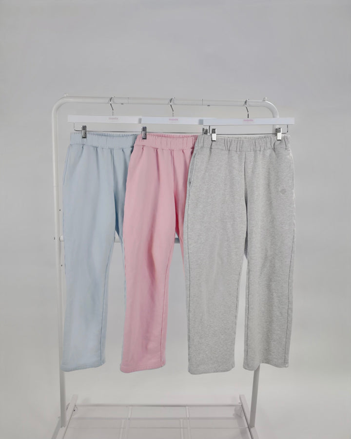 Three pairs of Bunny Sweatpants in light blue, pink, and gray hanging on a white clothing rack against a gray background