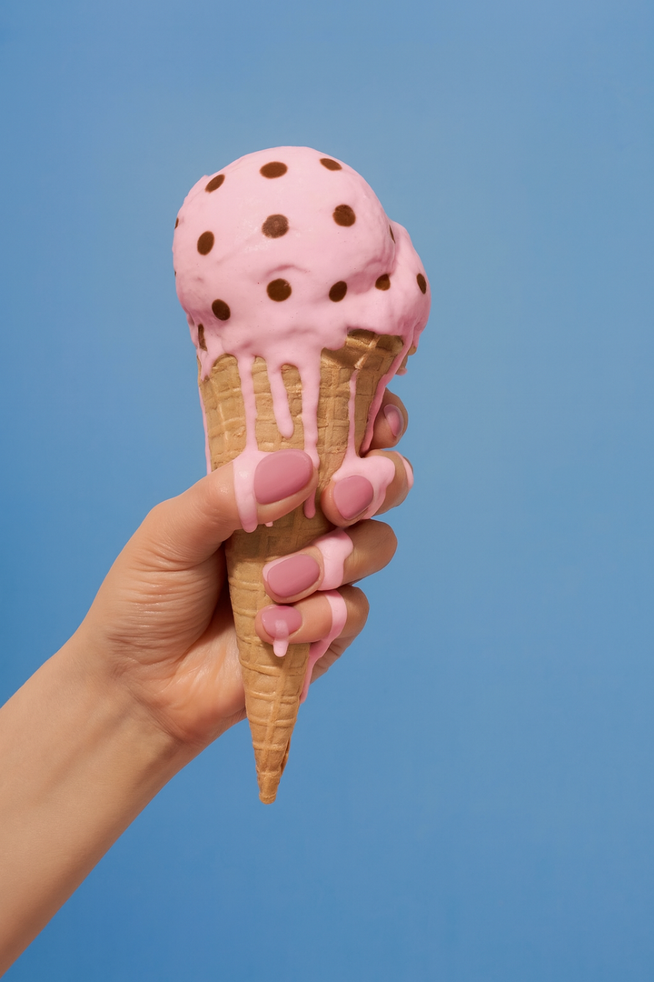Hand holding melting pink ice cream cone with chocolate chips against solid light blue background