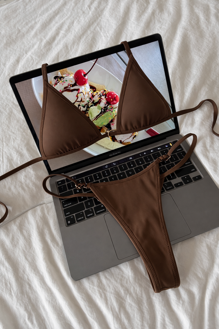 Brown triangle bikini top and thong bottoms laid flat on open laptop showing ice cream sundae image on screen