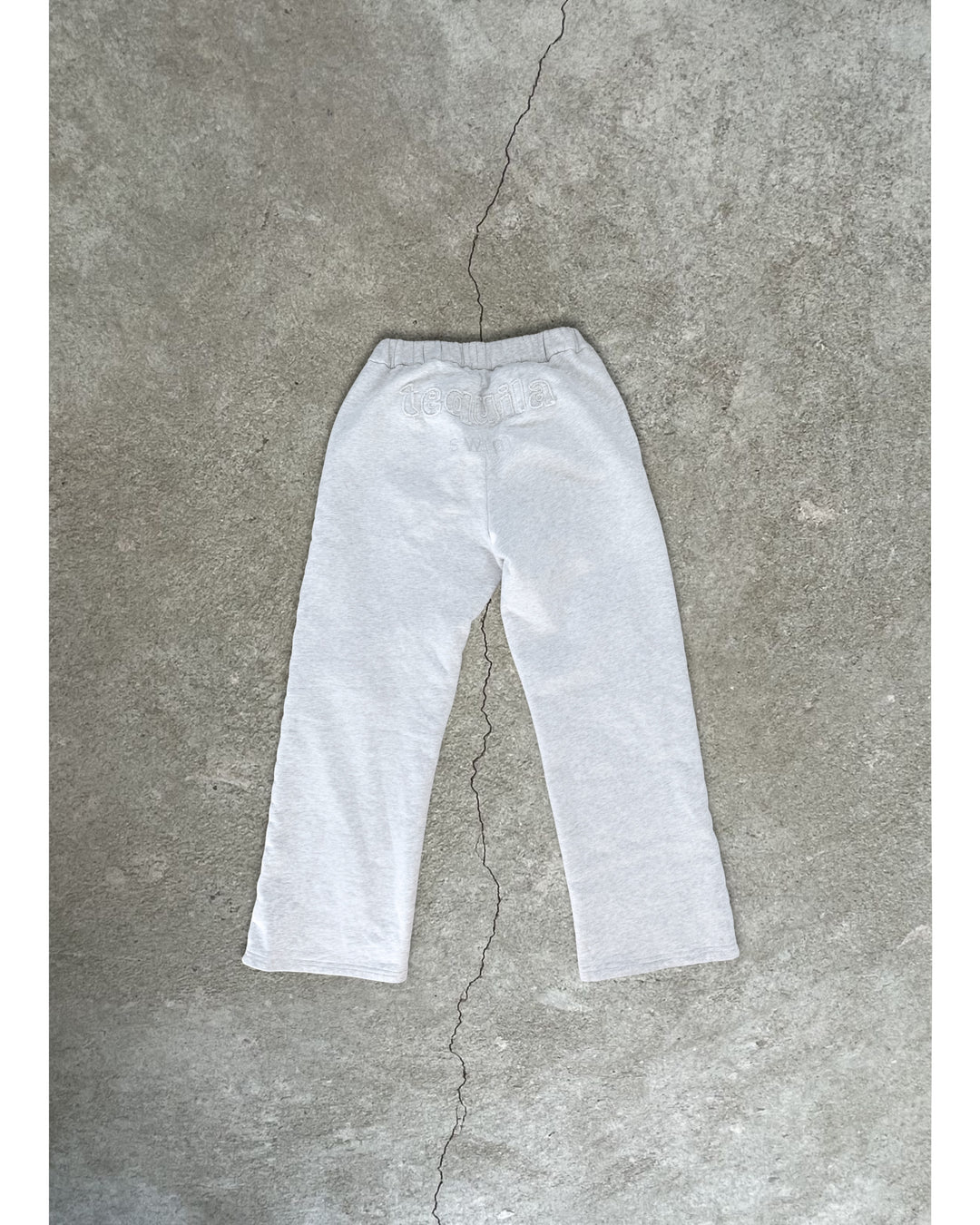 Light gray Bunny Sweatpants with elastic waistband laid flat on textured concrete floor background