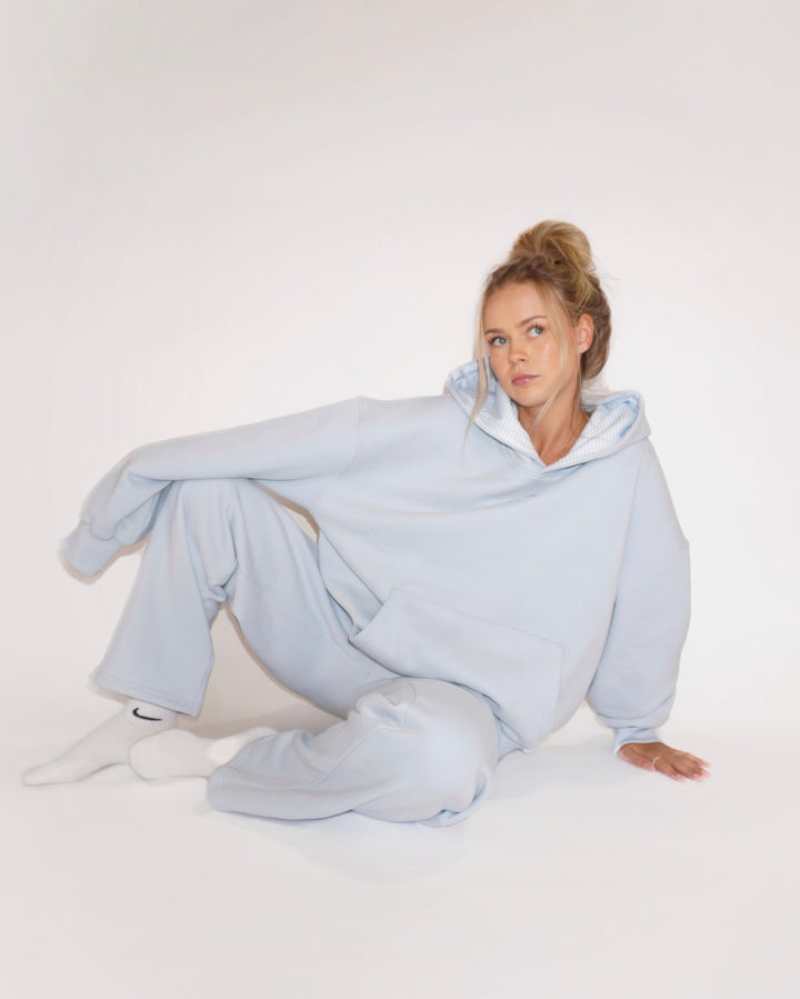Woman wearing light blue oversized hoodie and wide-leg Bunny Sweatpants sitting on white floor in relaxed pose