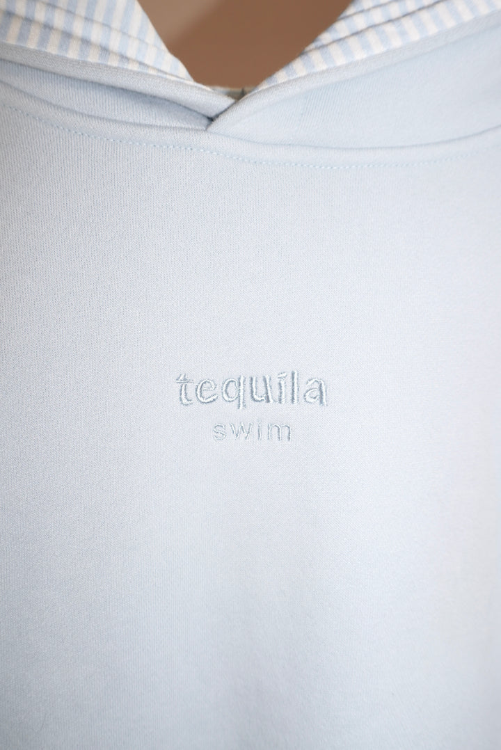Close-up of light blue Bunny Hug Hoodie with embroidered "tequila swim" logo on chest and striped inner hood lining