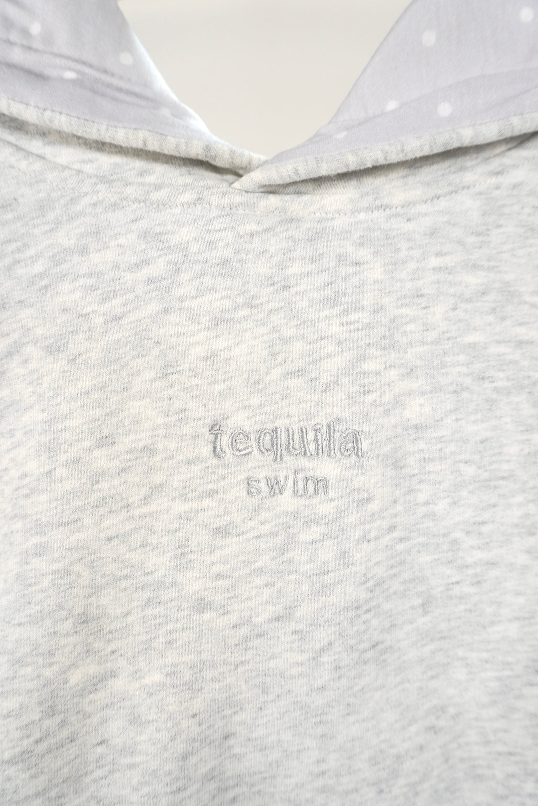 Close-up of light grey Bunny Hug Hoodie with "tequila swim" embroidered on the chest and polka dot hood lining visible
