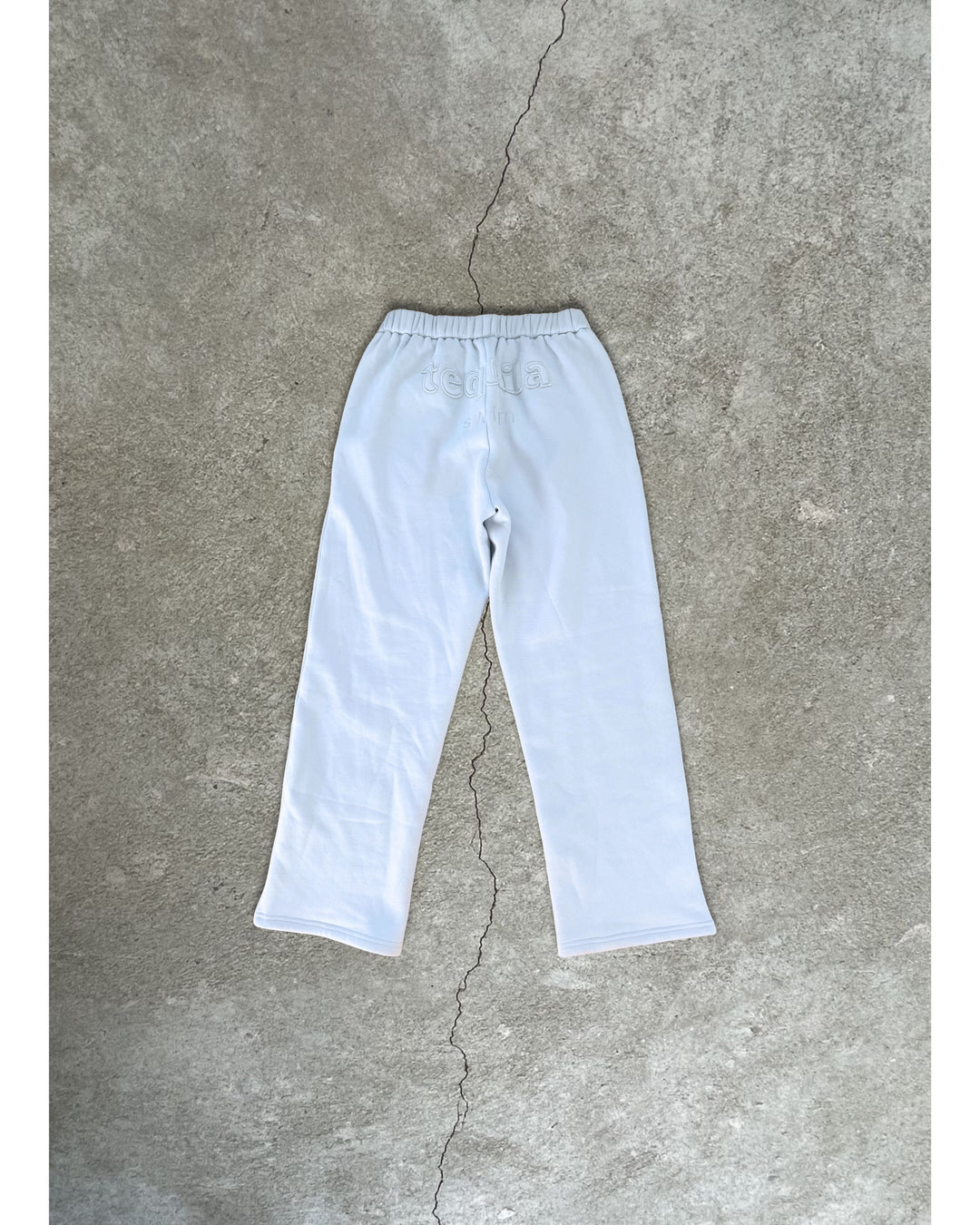 White bunny sweatpants with elastic waistband laid flat on a concrete floor with visible crack