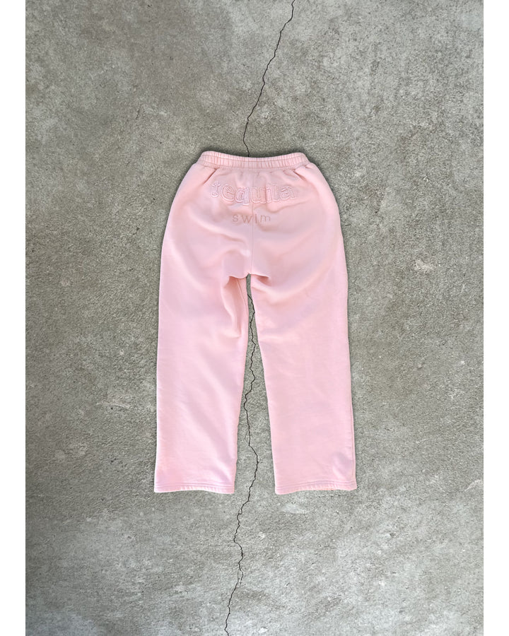 Soft pink Bunny Sweatpants laid flat on concrete background, featuring elastic waistband and back pocket detail.