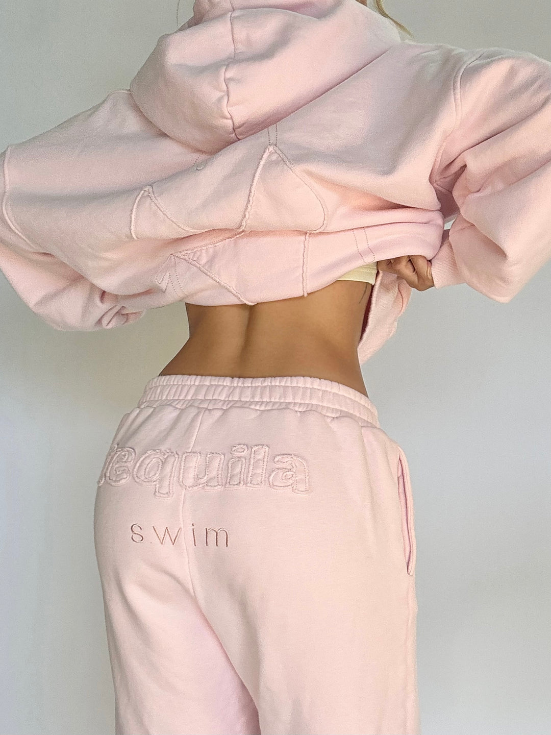 Back view of light pink Bunny Sweatpants with embroidered "Tequila swim" logo on the waistband worn with matching cropped hoodie