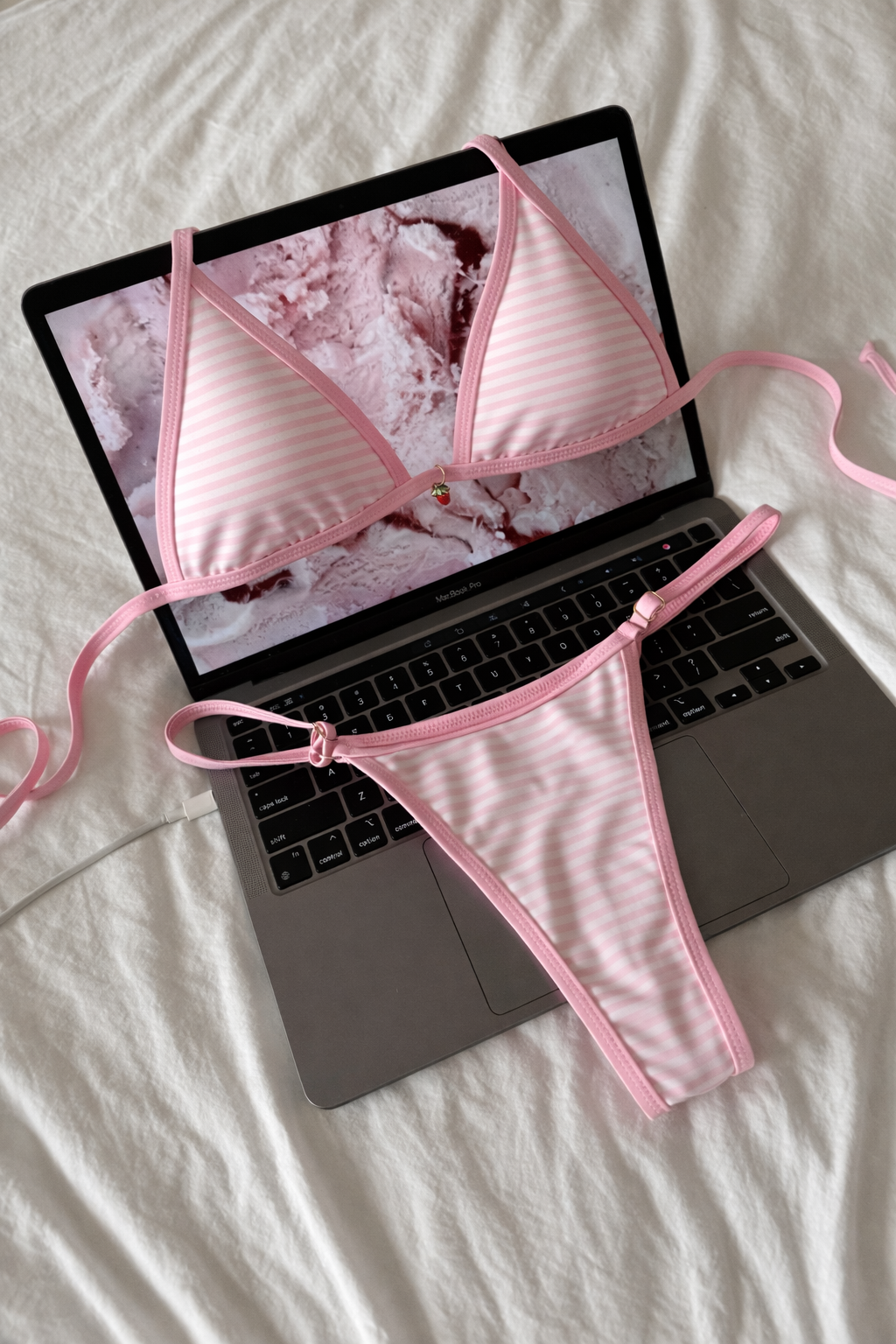 Pink bikini set draped over a laptop on a white surface