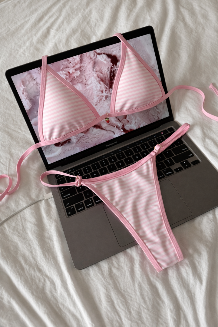 Pink bikini set draped over a laptop on a white surface