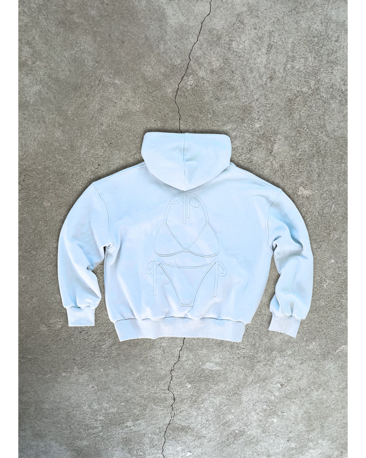 Light blue Bunny Hug Hoodie shown from the back with a stitched bikini design on the fabric against concrete background