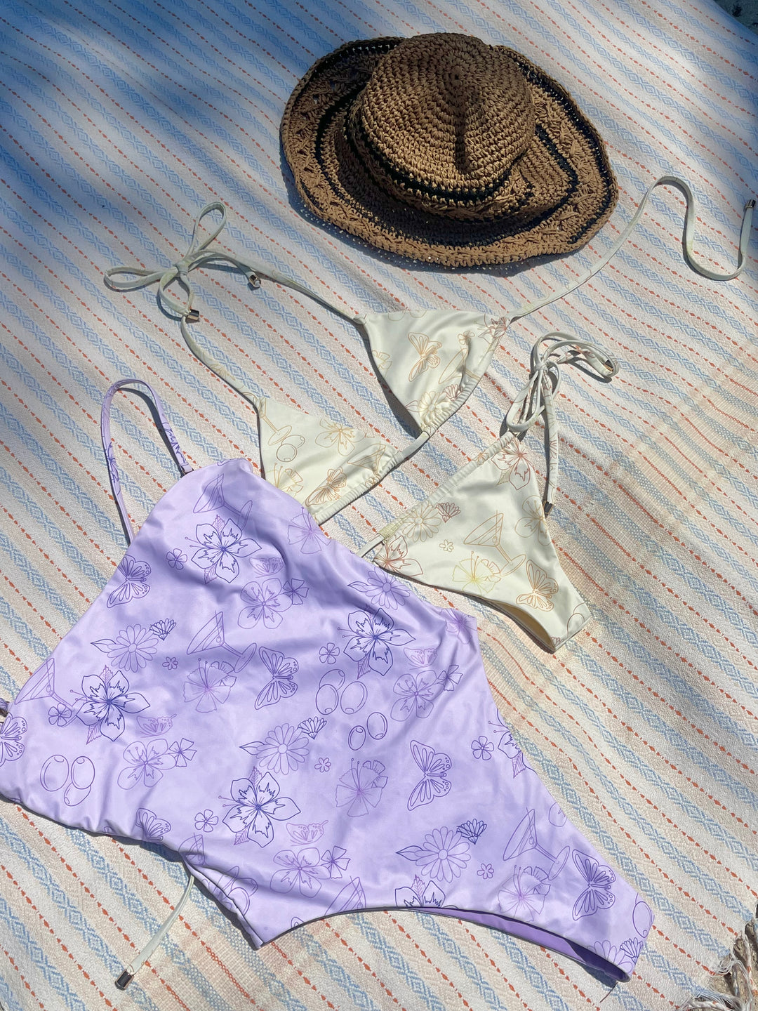 Straw sunhat, cream triangle bikini top with subtle pattern, and light purple floral print bikini bottom on striped fabric background