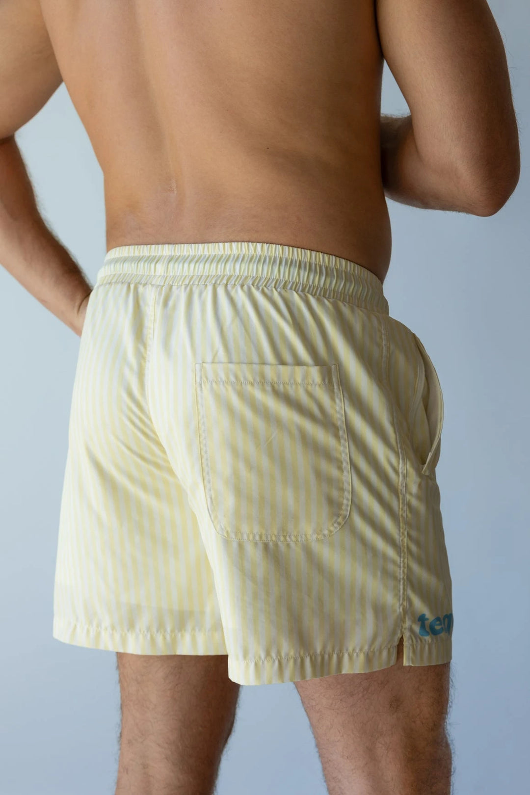 Man wearing light yellow and white vertical striped swim shorts with back pocket against plain background