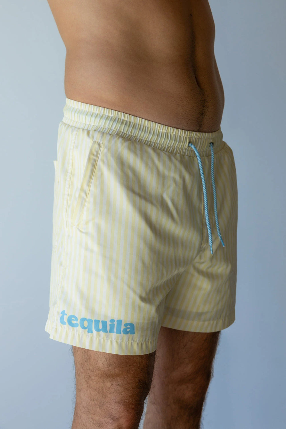 Light yellow swim shorts with thin vertical white stripes and blue drawstrings worn by man shown from waist to mid-thigh